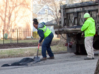 While she fills in potholes, her male coworker stands by.