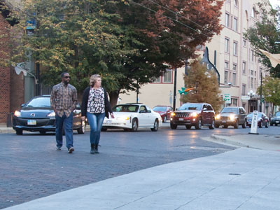 Clueless people jaywalk while a line of cars waits.