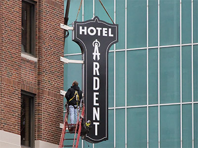 The sign is still hanging by a crane as the bolts are being drilled into the wall (see February 29, 2024).